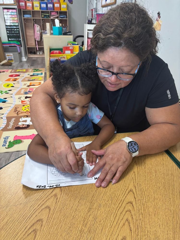 A teacher guiding a toddler's hand through letter tracing